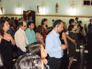 Some visually impaired guests wearing earphones and FM receptors are standing, watching the cerimony.