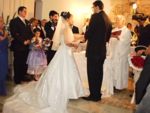 William and Adriana exchanging rings at the altar. Both wear intra-phone headset.