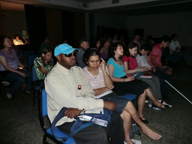 Foto de pessoas com deficiência visual assistindo ao filme NÁUFRAGO, no escurinho do cinema.