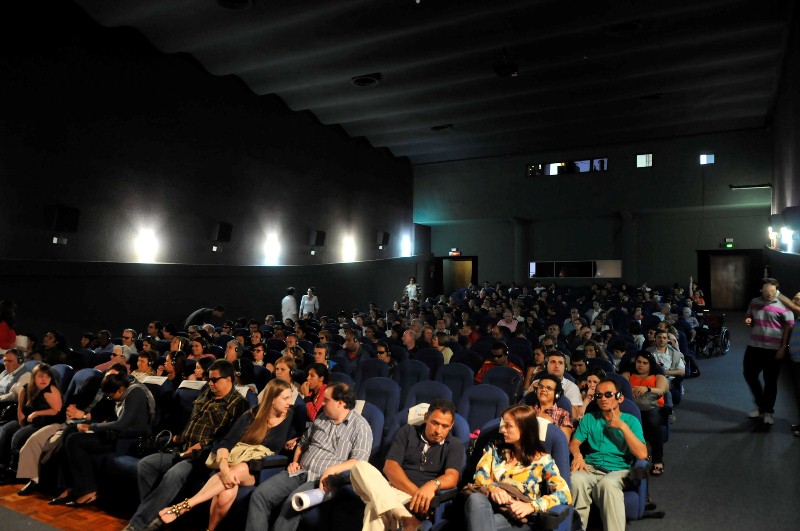 Fotografia colorida da sala do Cine Sabesp repleta de pessoas, antes da sessão.