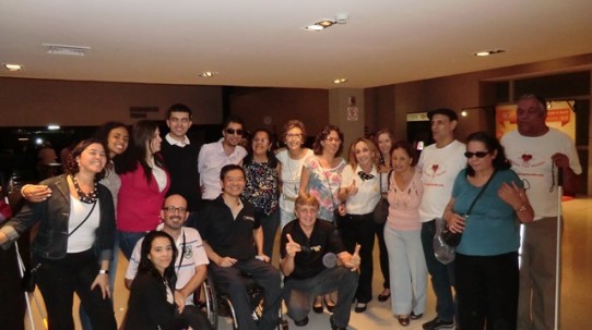 Fotografia colorida de várias pessoas com e sem deficiência, junto com o pessoal da VER COM PALAVRAS, no hall do HSBC Brasil.