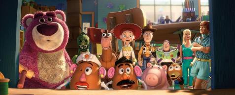 Foto colorida dos bonecos Woody, o cowboy, ao lado de Jessie e Buzz Lightyear com os amigos brinquedos.  Da esquerda para direita, o urso rosa Lotso, o dinossauro Rex, o cavalinho, Jessie, Woody, Buzz, o cachorro Slink, Barbie e Ken. À frente deles, o Sr. e Sra. Cabeça de Batata e o porquinho. Eles estão sorridentes, de pé, um ao lado do outro, no chão de uma sala.