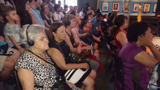 Fotografia colorida dos espectadores, alguns com fones de ouvido, aguardando o início do espetáculo Era uma Era. Da esquerda para direita, D. Lucinha, Marilene de Paula, Ângela Ribeiro, Edson Kadihara, Maria de Lourdes, Yasmin, William e Adriana Barsotti.