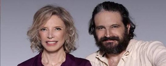 Fotografia em close dos atores Marília Gabriela e Caco Cioler, lado a lado, sorridentes. Marília, à esquerda,  é uma mulher de pele clara, com cabelos louros cacheados, na altura dos ombros, penteados de lado, rosto fino com traços delicados, olhos azuis e boca grande. Ela veste camisa cor de vinho e usa correntinha dourada com pingente. Caco, à direita, é um homem de pele clara, com cabelos pretos, com alguns fios grisalhos, penteados para trás, testa larga, olhos castanhos, pequenos e um pouco puxados, nariz largo, bigode e cavanhaque. Ele veste uma camisa bege.